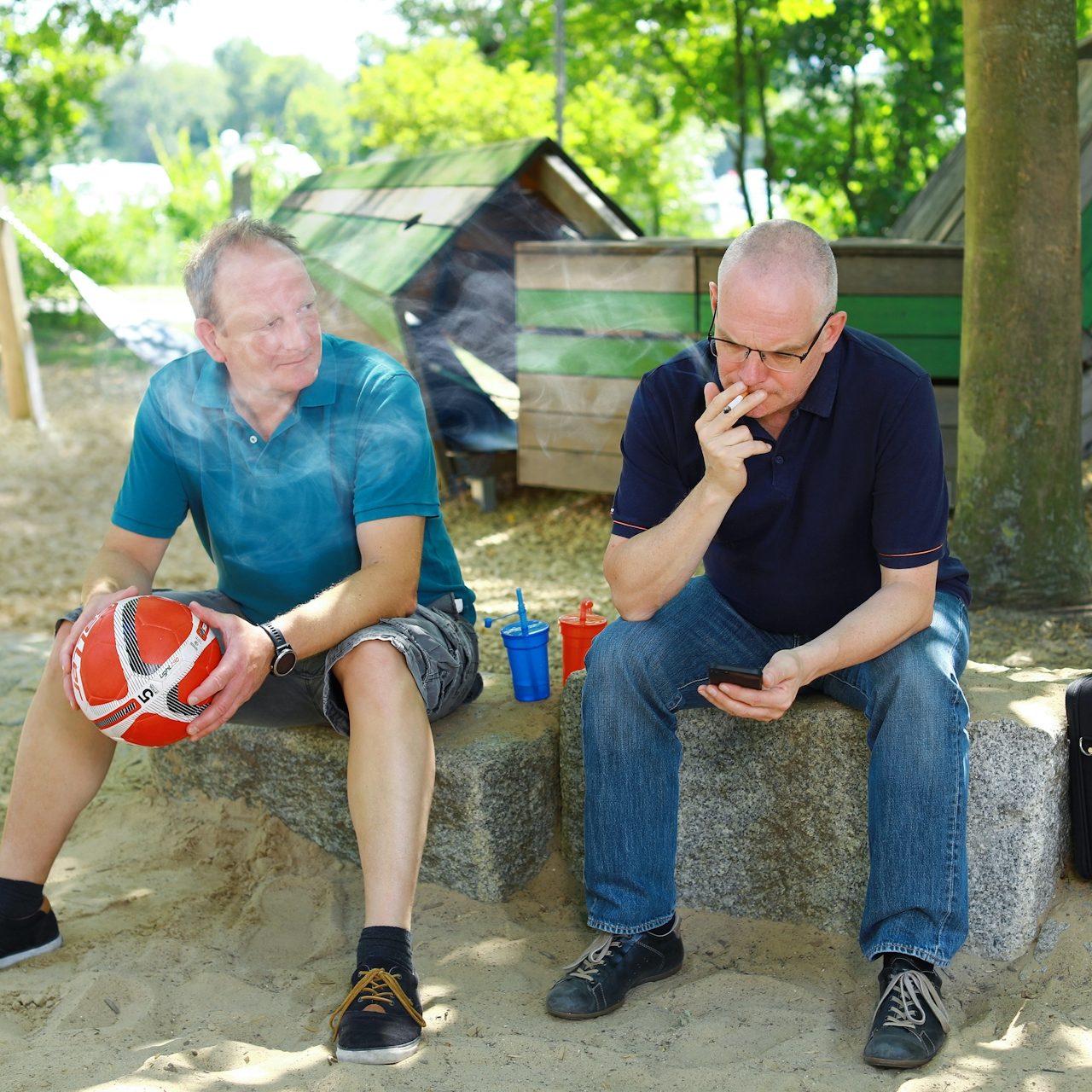 Raucher Zwei Männer sitzen im Freien auf einer Bank, einer hält einen Basketball in der Hand.